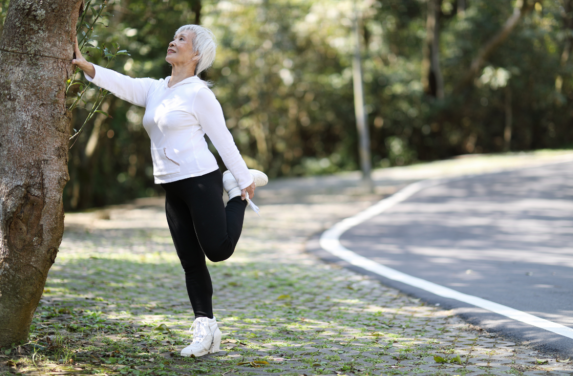 Stretching Over 60s female - thigh stretch. This stretch involves  standing tall with your feet hip-width apart. Take a moment to find your balance. Then, reach one hand back to grasp the ankle or top of the foot on the same side. Keep your knees close together and avoid arching your lower back excessively. Gently pull your heel towards your buttocks until you feel a comfortable stretch along the front of your thigh. Hold the stretch for 15-30 seconds while maintaining good posture and breathing deeply. Release the stretch and repeat on the opposite leg. This stretch helps to improve flexibility in the quadriceps, reduce muscle tension, and promote better overall mobility in the legs.